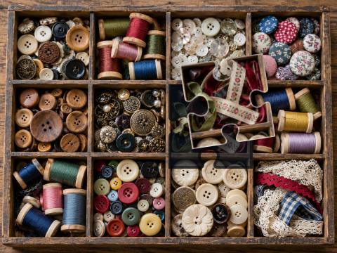Old wooden sorting tray filled with colorful buttons, thread spools and ribbons.