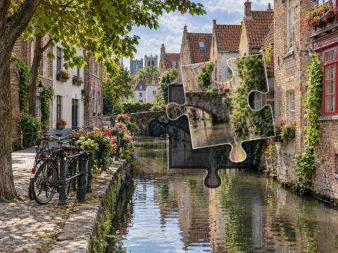 Old brick houses and a small arched bridge reflected in a canal beside a cobbled quay.